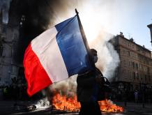 A protester waving a French national flag walks past a fire during clashes prior to the start of a demonstration to protest against the high cost of living, in Marseille, southern France, on October 17, 2026 as part of a nationwide call for mobilisation bringing together various groups expressing their anger: former Yellow Vests, secondary school and university students, climate activists and even farmers. After weeks of student protests, France faces broader, nationwide demonstrations on October 17, 2026 over the cost of living, setting up a potentially fraught six months heading into a presidential election. A police source told AFP that authorities estimated nearly 200,000 people could take part, with 40,000 in Paris. (Photo by Thibaud MORITZ / AFP)