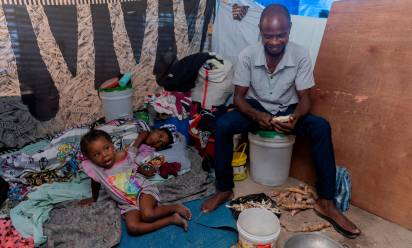 Un padre di famiglia sbuccia della manioca per nutrire le figlie, in un centro per sfollati, a Port-au-Prince. Foto Unicef